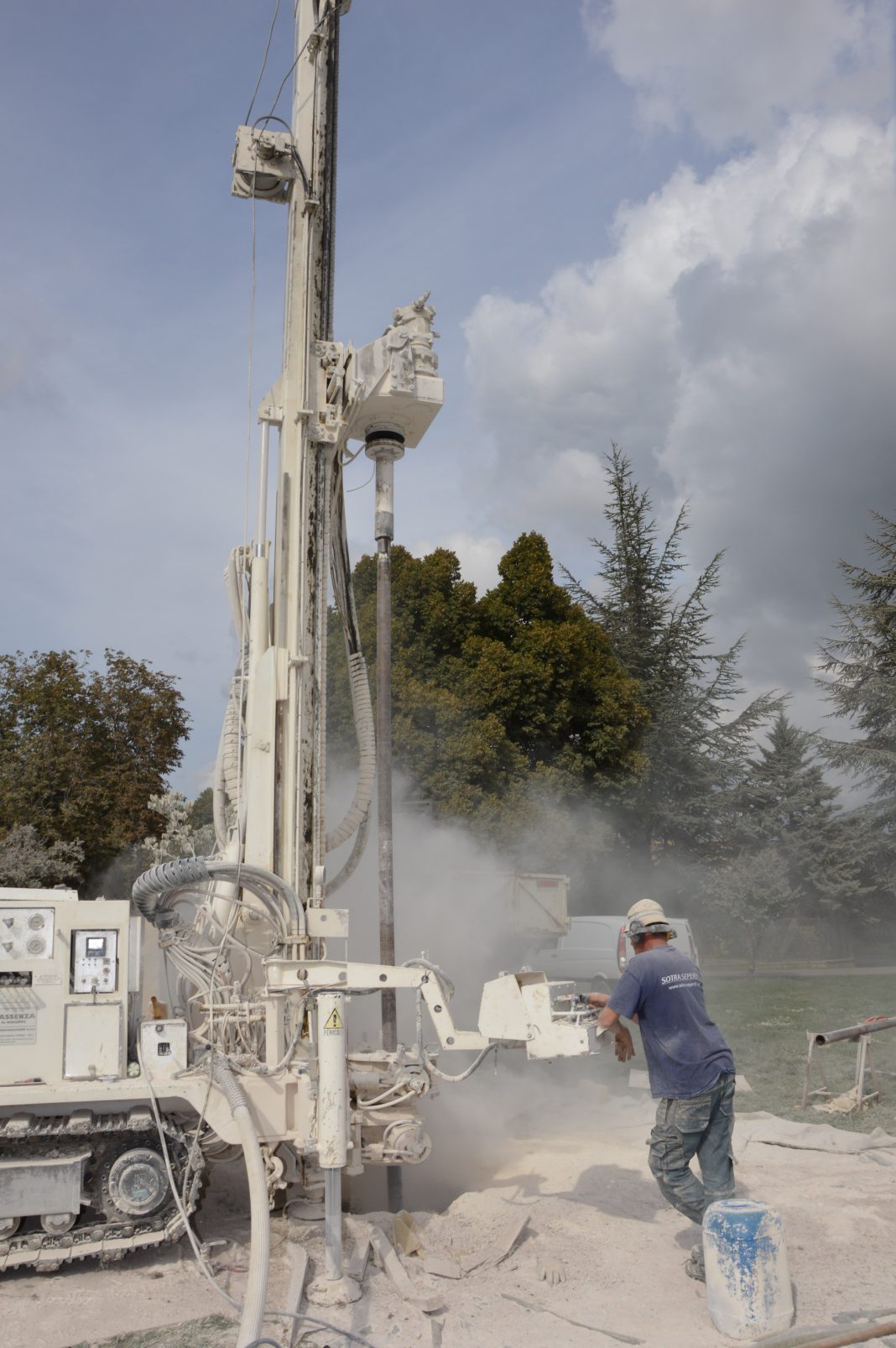 A worker operates a large industrial drilling rig outdoors on a cloudy day.